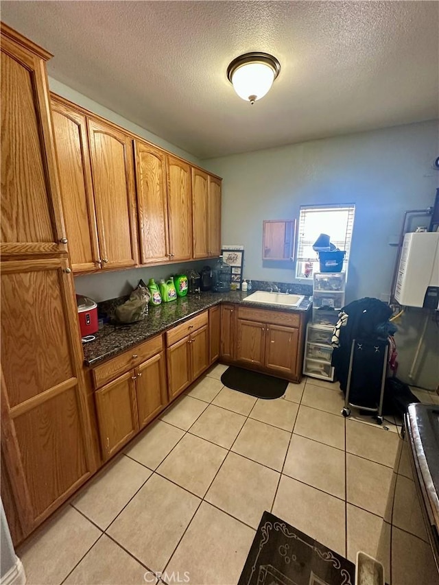 42500 20th St W, Lancaster, CA 93534 - kitchen with a textured ceiling, a sink, brown cabinetry, light tile patterned floors, and dark stone counters