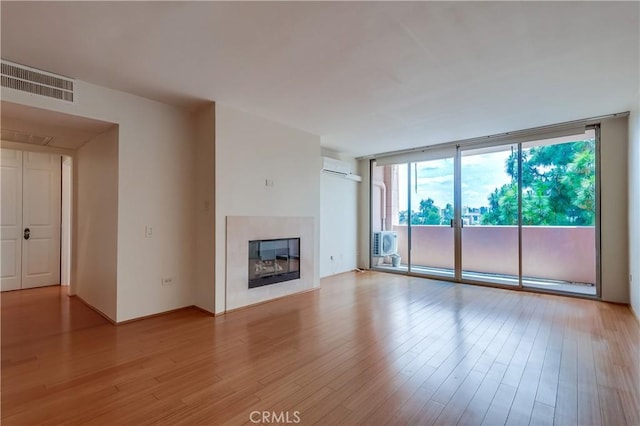 421 S La Fayette Park Pl Unit 701, Los Angeles, CA 90057 - unfurnished living room featuring a wall of windows, light wood finished floors, a glass covered fireplace, and a wall mounted air conditioner