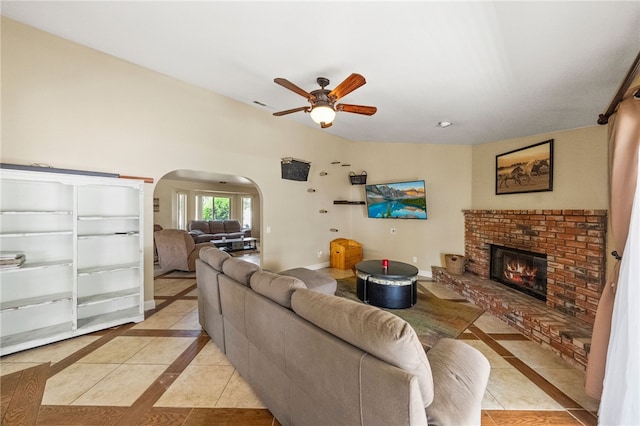 32642 Durango Ct, Wildomar, CA 92595 - living room featuring arched walkways, inlaid floor details, a ceiling fan, a brick fireplace, and light tile patterned floors