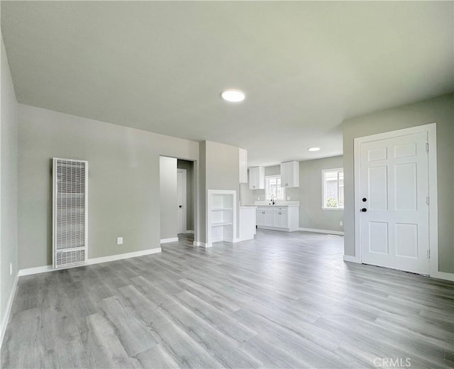 1976 E 112th St, Los Angeles, CA 90059 - unfurnished living room with a heating unit, baseboards, light wood finished floors, recessed lighting, and a sink