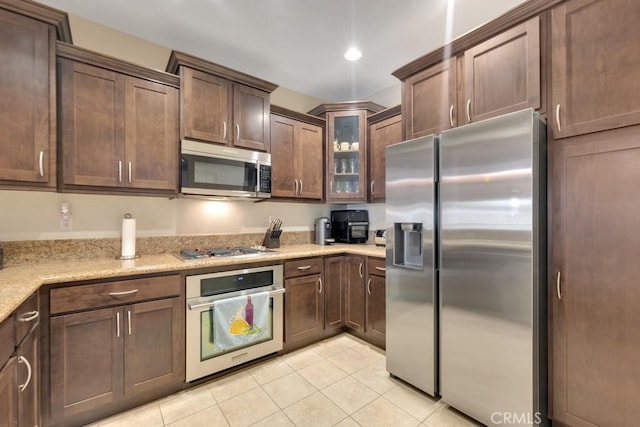 13200 Moorpark St Unit 201, Sherman Oaks, CA 91423 - kitchen featuring stainless steel appliances, light tile patterned floors, glass insert cabinets, light stone counters, and dark brown cabinets