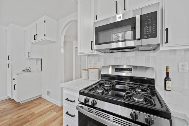 3581 Cameo Dr Unit 35, Oceanside, CA 92056 - kitchen featuring appliances with stainless steel finishes, arched walkways, white cabinets, light stone counters, and light wood-style flooring