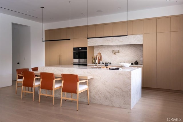 16828 Otsego St, Encino, CA 91436 - kitchen featuring stainless steel double oven, light wood-style floors, a large island with sink, modern cabinets, and light stone counters