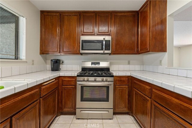 42330 61st St W, Lancaster, CA 93536 - kitchen with stainless steel appliances, light countertops, light tile patterned floors, and brown cabinets