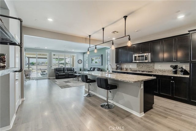 29042 Botanical Cir, Menifee, CA 92584 - kitchen with stainless steel microwave, gas cooktop, open floor plan, light wood-style floors, and a kitchen breakfast bar