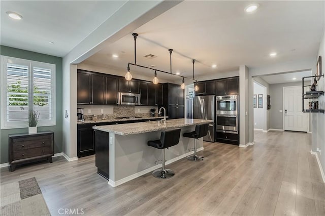 29042 Botanical Cir, Menifee, CA 92584 - kitchen with stainless steel appliances, light stone countertops, tasteful backsplash, light wood finished floors, and baseboards