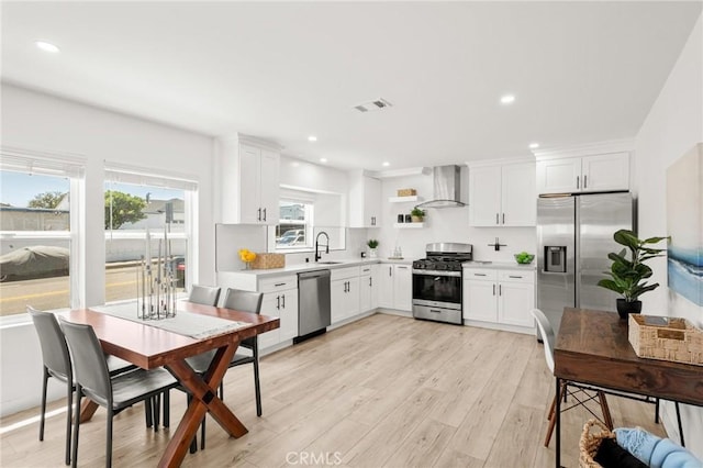 453 N Walker Ave, San Pedro, CA 90732 - kitchen with stainless steel appliances, wall chimney exhaust hood, a sink, white cabinets, and light wood-style flooring