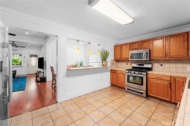 1040 W 3rd St, Pomona, CA 91766 - kitchen featuring stainless steel appliances, backsplash, brown cabinetry, crown molding, and light tile patterned floors