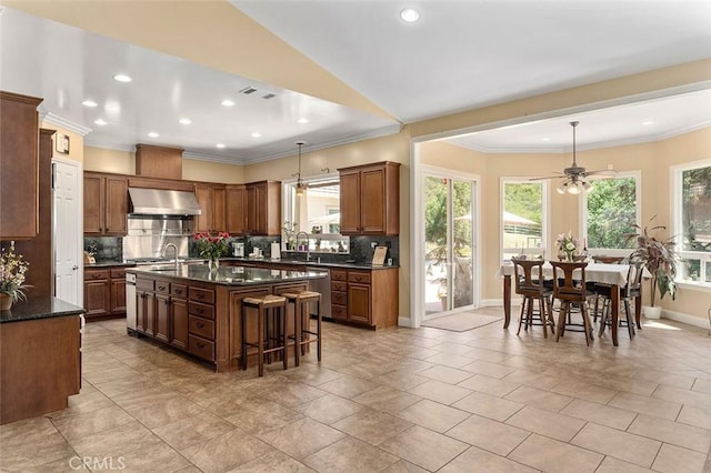 41275 Hacienda Dr, Murrieta, CA 92562 - kitchen with wall chimney range hood, a center island with sink, backsplash, a kitchen breakfast bar, and a ceiling fan