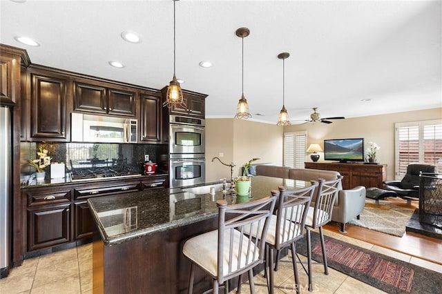 40678 Alondra Dr, Murrieta, CA 92562 - kitchen featuring appliances with stainless steel finishes, tasteful backsplash, a kitchen breakfast bar, light tile patterned flooring, and dark stone countertops