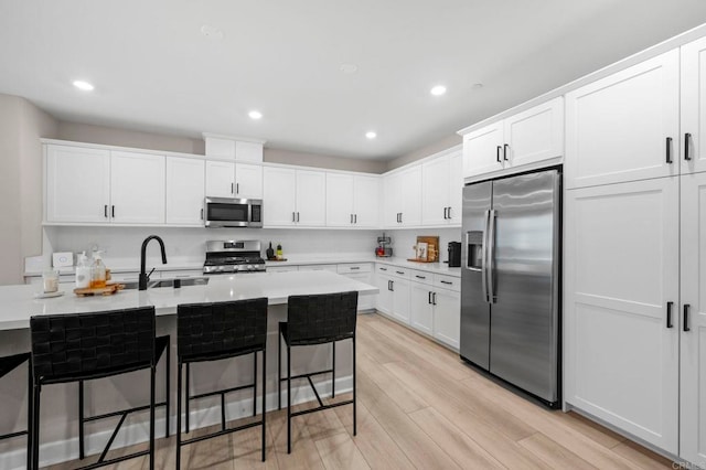 7902 Belluno Way, San Diego, CA 92126 - kitchen with appliances with stainless steel finishes, a sink, light wood-style flooring, a kitchen bar, and white cabinetry