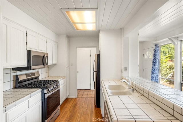 2631 San Jose St, Chico, CA 95973 - kitchen with appliances with stainless steel finishes, tile counters, a sink, white cabinetry, and light wood-type flooring
