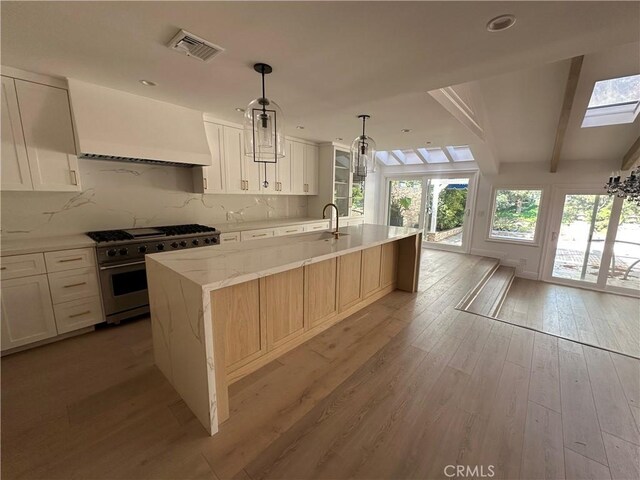 23128 Park Sorrento, Calabasas, CA 91302 - kitchen featuring high end stove, light wood-style flooring, a kitchen island with sink, light stone counters, and decorative backsplash