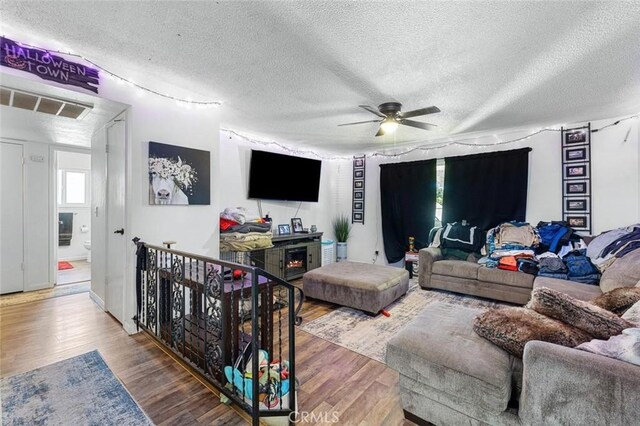 2192 Beverly Ave, Clovis, CA 93611 - living room with wood finished floors, a textured ceiling, a ceiling fan, and a lit fireplace