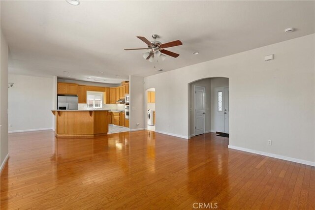 1095 Glenwood Ln, Willows, CA 95988 - unfurnished living room featuring arched walkways, a ceiling fan, light wood finished floors, baseboards, and washer / clothes dryer