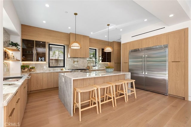 22640 Clarendon St, Woodland Hills, CA 91367 - kitchen featuring stainless steel built in refrigerator, modern cabinets, a kitchen island with sink, backsplash, and light wood finished floors