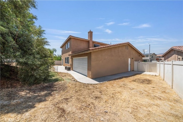 1568 Burns Ln, San Jacinto, CA 92335 - view of property exterior with stucco siding, a chimney, a garage, a fenced backyard, and cooling unit