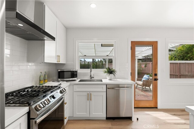 3145 Sicily Ave, Costa Mesa, CA 92626 - kitchen featuring appliances with stainless steel finishes, wall chimney exhaust hood, a sink, light wood finished floors, and backsplash