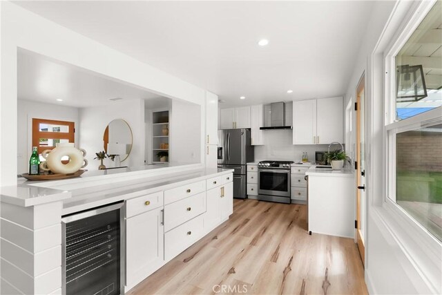 3145 Sicily Ave, Costa Mesa, CA 92626 - kitchen featuring appliances with stainless steel finishes, wine cooler, wall chimney range hood, white cabinetry, and light countertops