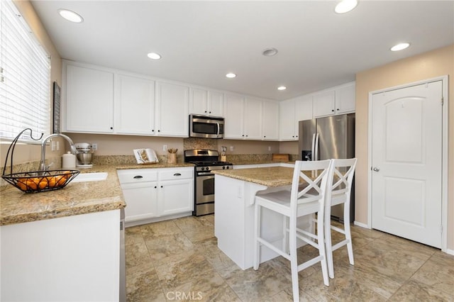 29304 Riptide Dr, Menifee, CA 92585 - kitchen with stainless steel appliances, white cabinets, a sink, a breakfast bar area, and a center island