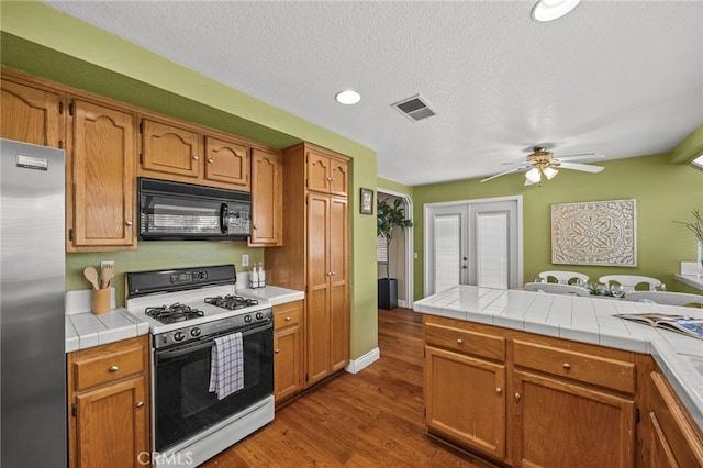 14252 Parkside Ct, Chino Hills, CA 91709 - kitchen with black microwave, range with gas stovetop, stainless steel refrigerator, dark wood-style flooring, and ceiling fan
