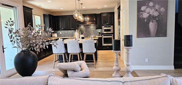 29310 Paseo Palmar, San Juan Capistrano, CA 92675 - kitchen featuring light wood-style flooring, dark cabinets, tasteful backsplash, a kitchen breakfast bar, and recessed lighting