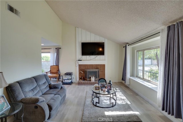 12076 Racket Ct, Moreno Valley, CA 92557 - living room featuring light wood-style flooring, a textured ceiling, a brick fireplace, and high vaulted ceiling