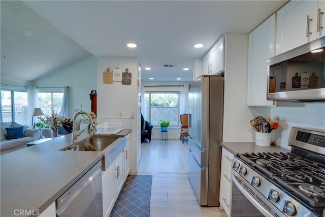 12076 Racket Ct, Moreno Valley, CA 92557 - kitchen with appliances with stainless steel finishes, a sink, open floor plan, white cabinetry, and vaulted ceiling