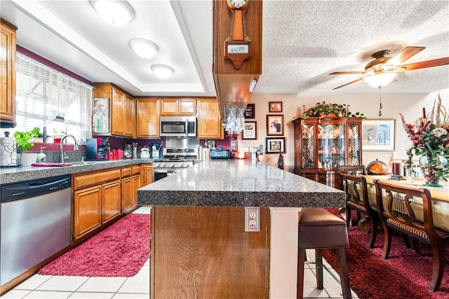5471 E Centralia St Unit 24, Long Beach, CA 90808 - kitchen with stainless steel appliances, a peninsula, a breakfast bar, a sink, and brown cabinetry