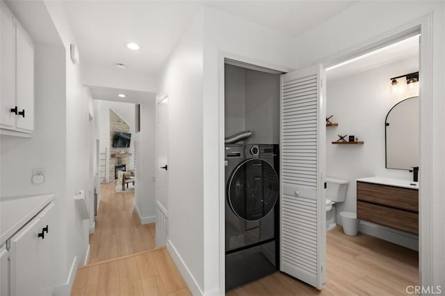 20092 Bayfront Ln Unit 206, Huntington Beach, CA 92646 - laundry room featuring washer / clothes dryer, light wood-type flooring, a stone fireplace, baseboards, and recessed lighting