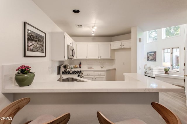 2759 Butter Creek Dr, Pasadena, CA 91107 - kitchen featuring stainless steel microwave, a peninsula, backsplash, white cabinets, and a breakfast bar area