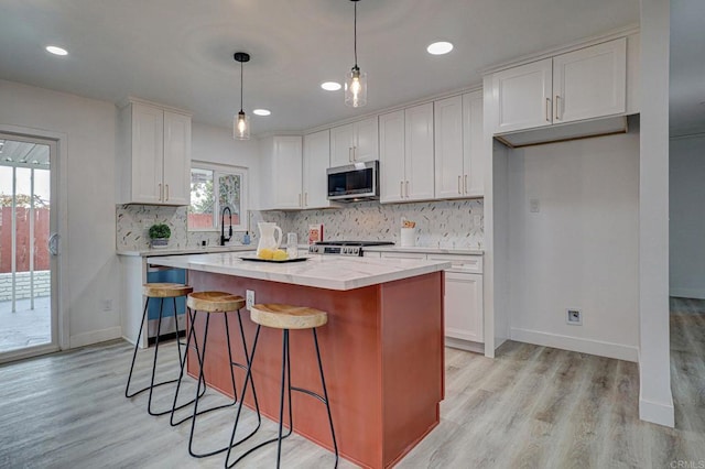 1320 Vinca Way, San Diego, CA 92114 - kitchen with stainless steel microwave, a center island, white cabinetry, decorative backsplash, and light wood finished floors