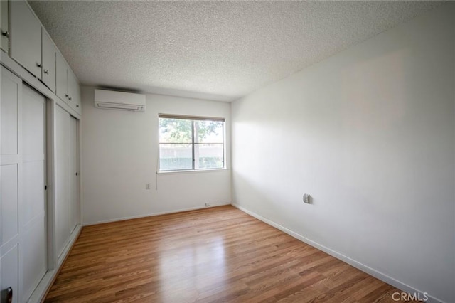 270 Avenida Sevilla Unit C, Laguna Woods, CA 92637 - unfurnished bedroom with wood finished floors, a wall mounted AC, a textured ceiling, a closet, and baseboards