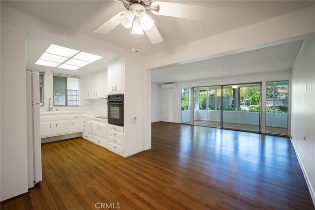 270 Avenida Sevilla Unit C, Laguna Woods, CA 92637 - kitchen featuring black oven, a wall unit AC, dark wood finished floors, open floor plan, and white cabinetry