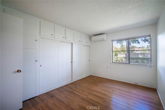 270 Avenida Sevilla Unit C, Laguna Woods, CA 92637 - unfurnished bedroom with a wall mounted AC, wood finished floors, a textured ceiling, a closet, and baseboards