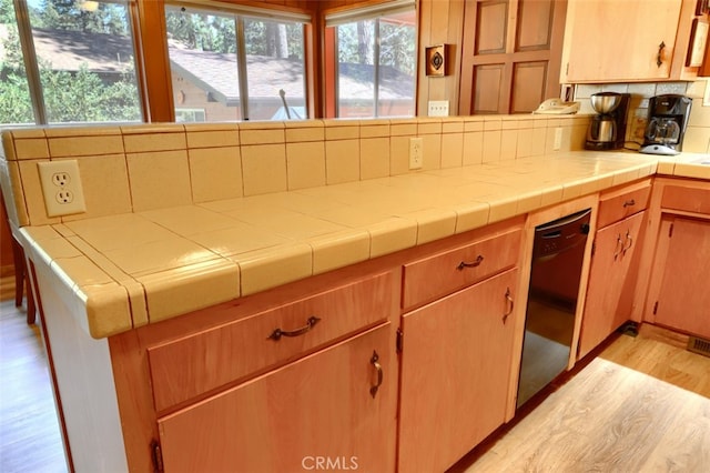 8067 Chilnualna Falls Rd, Wawona, CA 95389 - kitchen featuring black dishwasher, light wood-style floors, backsplash, a peninsula, and tile countertops