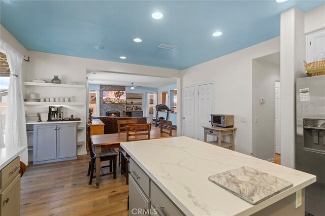 3042 San Luis Dr, Lancaster, CA 93535 - kitchen with stainless steel fridge, light stone countertops, light wood-type flooring, a warm lit fireplace, and a ceiling fan