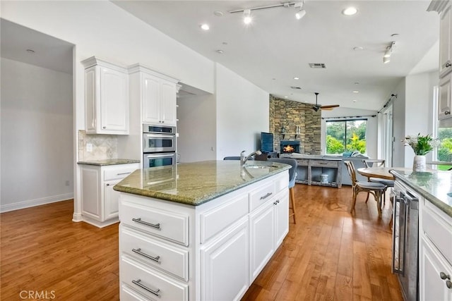 1177 Estee Ct, Fallbrook, CA 92028 - kitchen with open floor plan, stainless steel double oven, light wood-style floors, a ceiling fan, and light stone counters