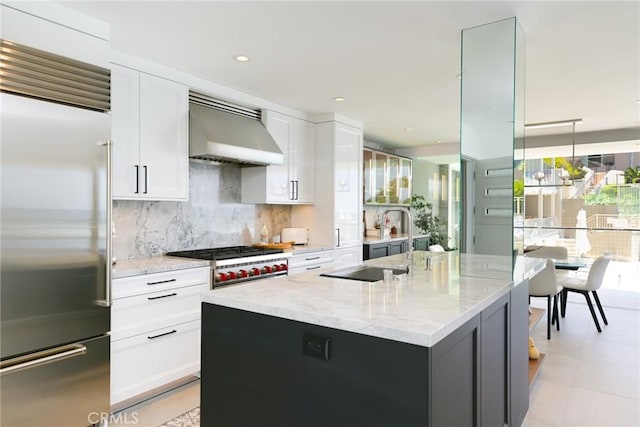 1585 S Coast Unit 2, Laguna Beach, CA 92651 - kitchen featuring stainless steel built in fridge, wall chimney range hood, tasteful backsplash, light stone counters, and an island with sink