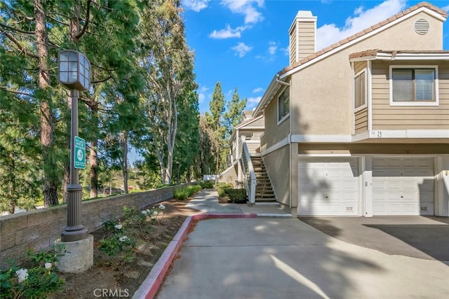 56 Coventry Ln Unit 293, Aliso Viejo, CA 92656 - view of side of property featuring stucco siding, a chimney, a tiled roof, a garage, and driveway