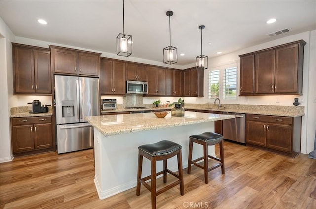 34197 Helenium St, Murrieta, CA 92563 - kitchen with appliances with stainless steel finishes, dark brown cabinetry, light wood-style flooring, a center island, and hanging light fixtures