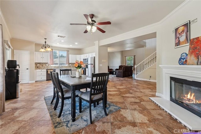 7538 N Erie Ave, Fresno, CA 93722 - dining room with a ceiling fan, crown molding, a glass covered fireplace, stairs, and a chandelier