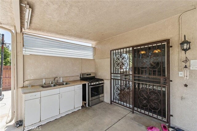 7538 N Erie Ave, Fresno, CA 93722 - kitchen with stainless steel gas range, concrete floors, a textured wall, white cabinetry, and light countertops