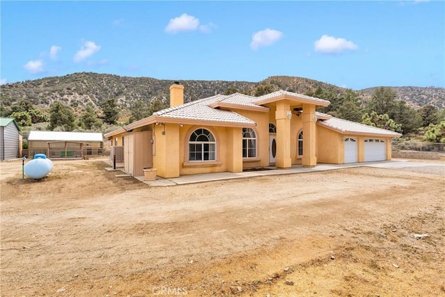 1679 Desert Front Rd, Wrightwood, CA 92397 - view of front of home featuring a chimney, a mountain view, a tiled roof, stucco siding, and an attached garage