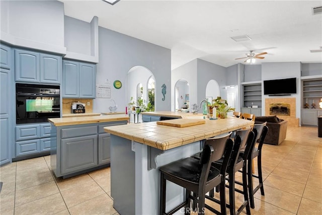 1679 Desert Front Rd, Wrightwood, CA 92397 - kitchen featuring black oven, a center island with sink, light tile patterned flooring, a ceiling fan, and vaulted ceiling