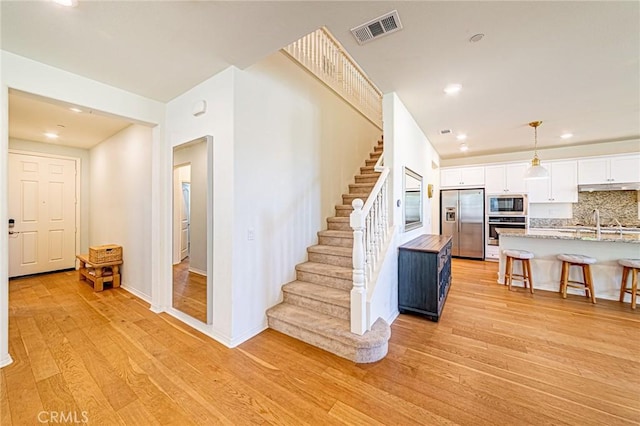 24207 Via Perla, Valencia, CA 91354 - kitchen with appliances with stainless steel finishes, a kitchen breakfast bar, white cabinets, light wood-style flooring, and decorative backsplash