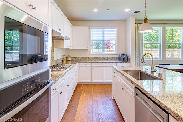 24207 Via Perla, Valencia, CA 91354 - kitchen featuring appliances with stainless steel finishes, a sink, under cabinet range hood, light wood finished floors, and white cabinets