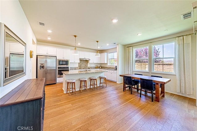 24207 Via Perla, Valencia, CA 91354 - kitchen featuring appliances with stainless steel finishes, white cabinets, light wood-style flooring, a breakfast bar area, and an island with sink