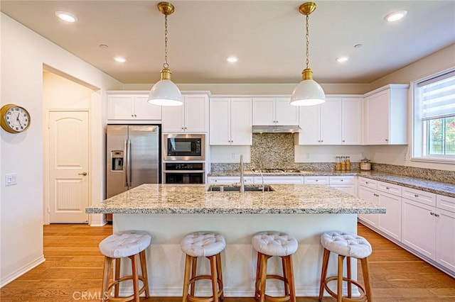 24207 Via Perla, Valencia, CA 91354 - kitchen featuring appliances with stainless steel finishes, under cabinet range hood, a sink, a kitchen bar, and white cabinetry