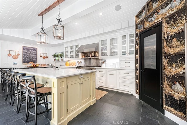 105 Via Waziers, Newport Beach, CA 92663 - kitchen with wall chimney exhaust hood, lofted ceiling, a breakfast bar area, glass insert cabinets, and a large island
